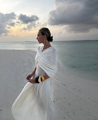 Woman in a white dress standing on a beach with a sunset in the background
