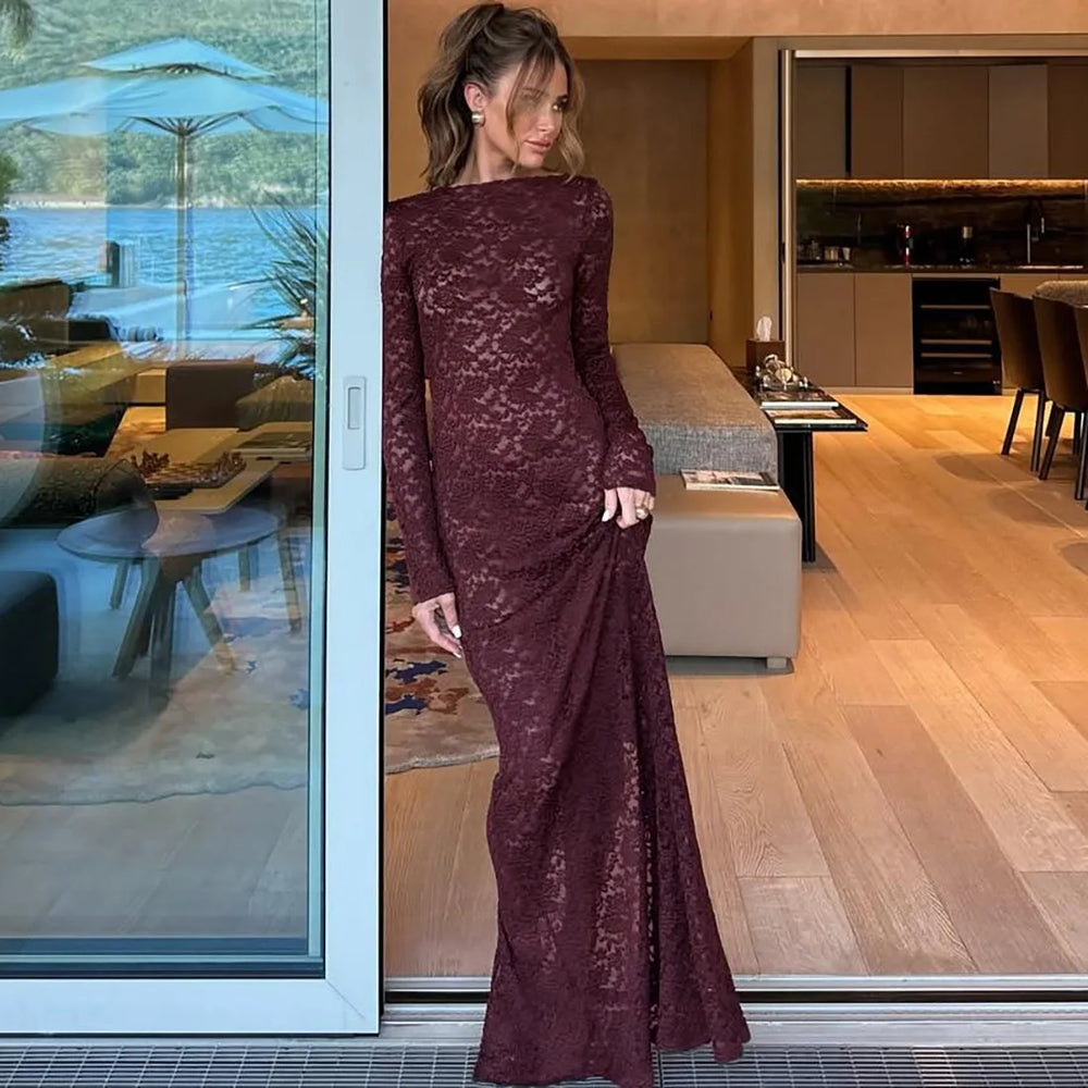 Woman in a burgundy lace dress standing in a modern indoor setting with a view of water outside.