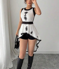 Woman wearing a white dress with black floral embroidery and knee-high boots in a minimal indoor setting.