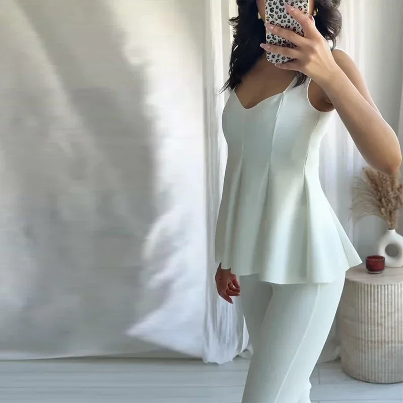 Person wearing a white sleeveless top and pants in a minimalistic room.