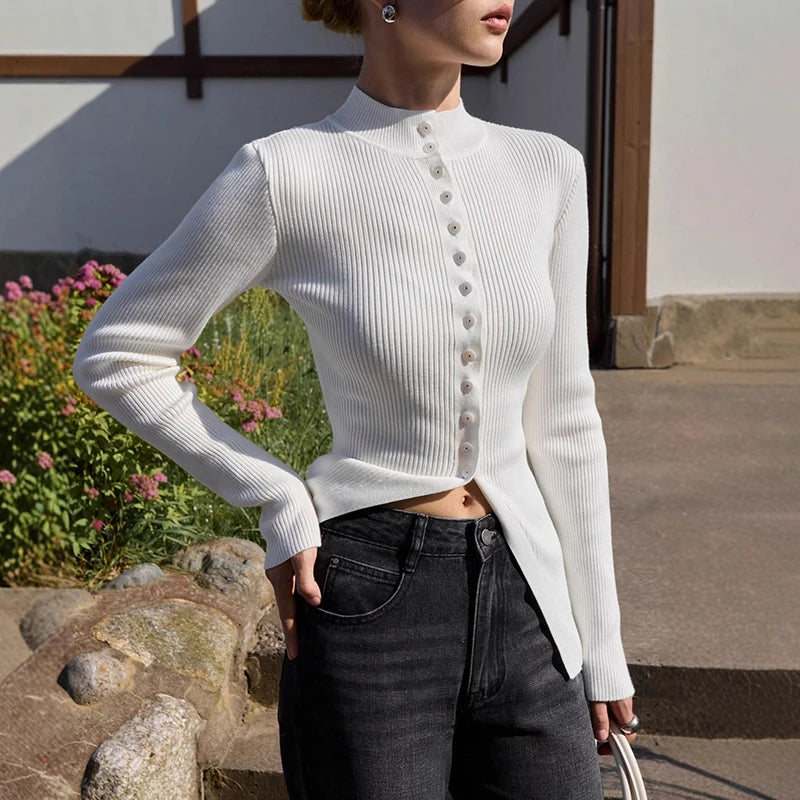 Person wearing a white ribbed sweater with button details outdoors.