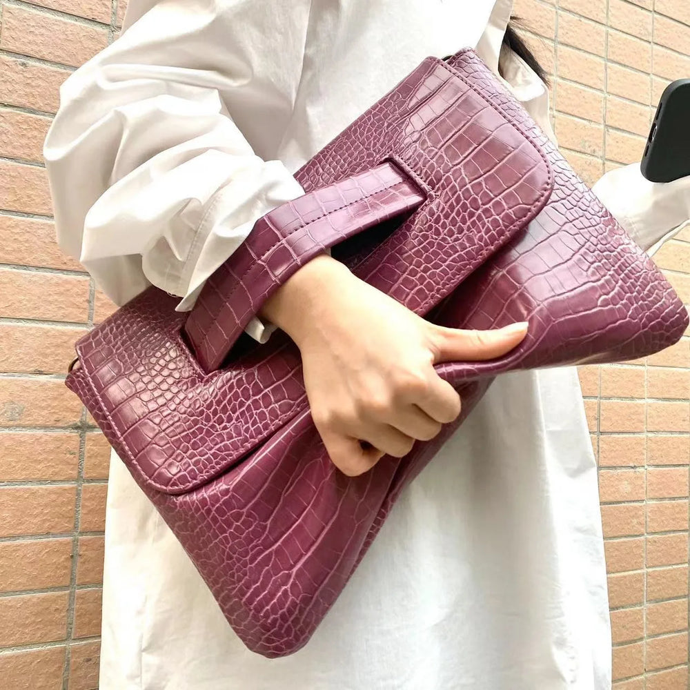 Person holding a purple crocodile-patterned handbag against a brick wall.