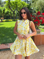 Woman in a yellow floral dress standing in a garden with green grass and red flowers.