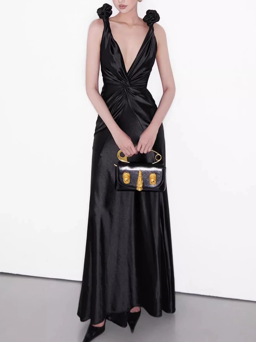 Woman in a black satin dress holding a matching handbag against a white background