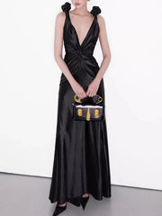 Woman in a black satin dress holding a matching handbag against a white background