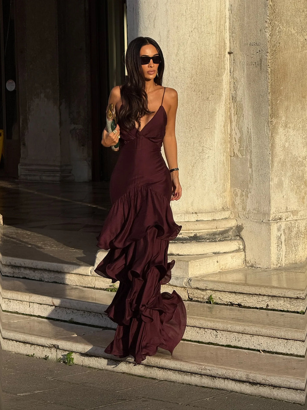 Woman in a burgundy dress standing on stone steps with classical architecture in the background