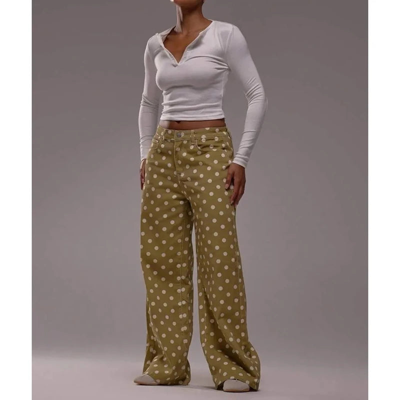 Woman wearing a white long-sleeve top and green polka dot pants on a gray background