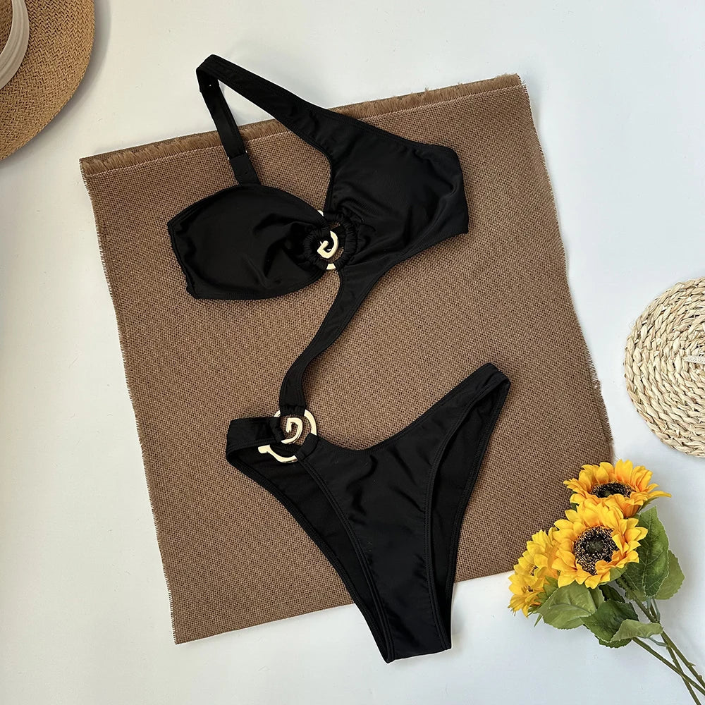 Black one piece swimsuit with asymmetrical strap and gold hardware laid flat