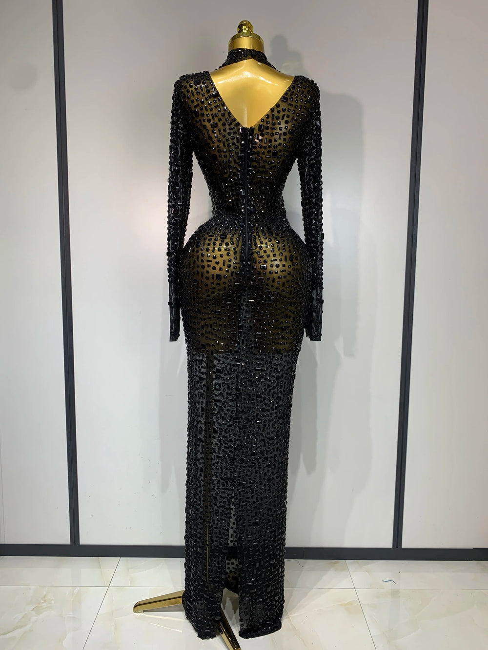 Black beaded evening gown on a mannequin against a white wall.