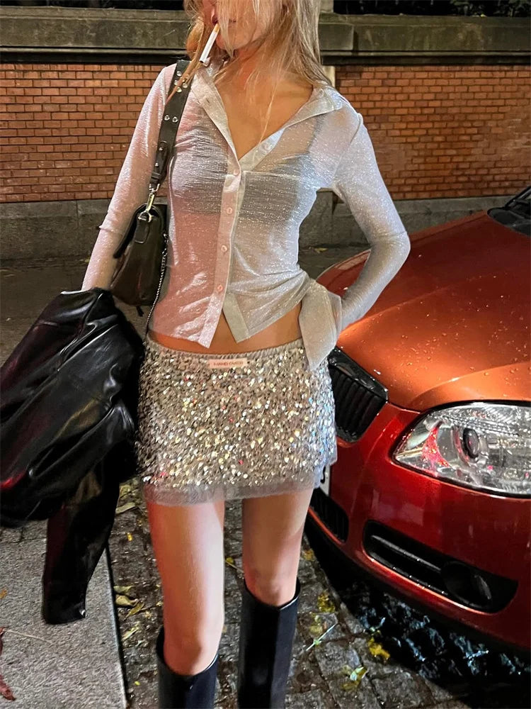 Person in a sequin skirt standing next to a red car on a street.