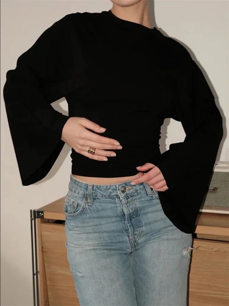 Person wearing a black cropped sweater with ruffled sleeves and light blue jeans.