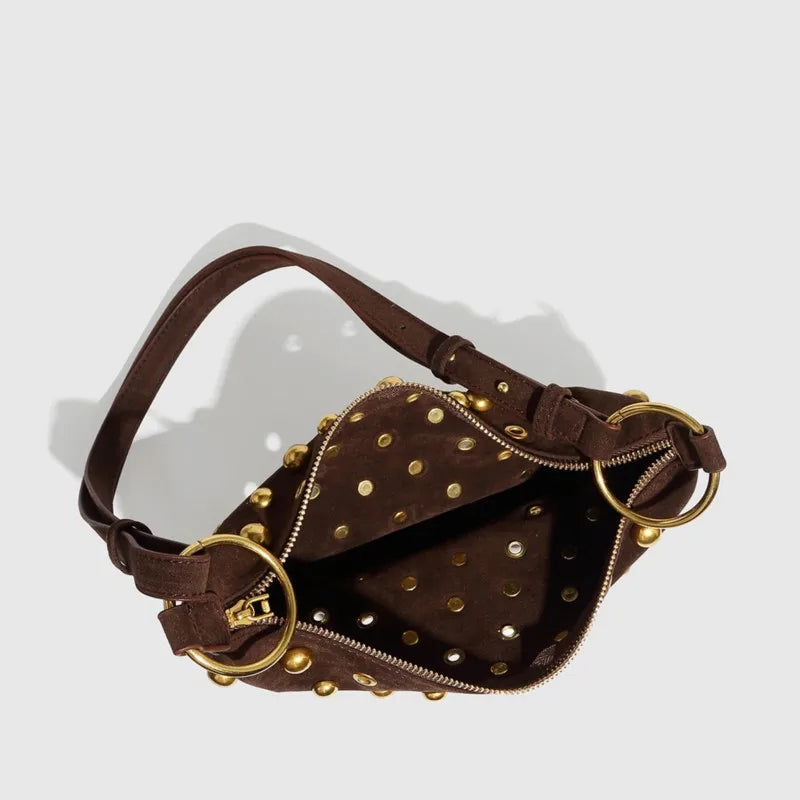 Brown leather bag with gold studs and rings on a light gray background