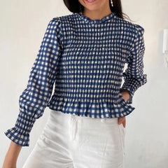 Woman wearing a blue and white checkered blouse with ruffled sleeves against a plain background