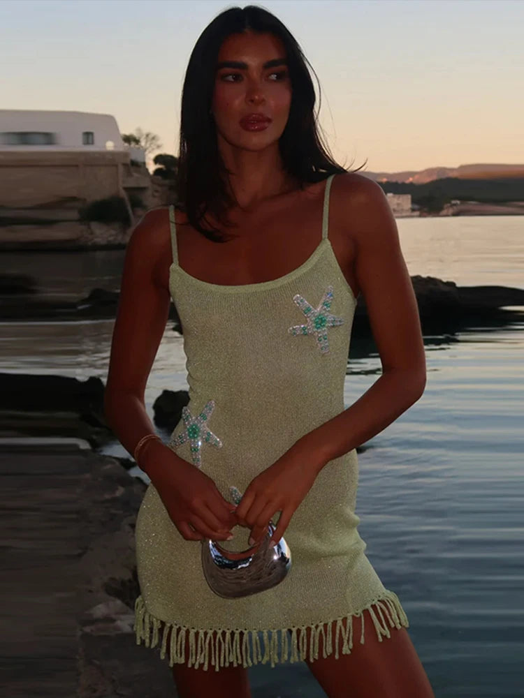 Woman in a light green dress with starfish designs standing by a body of water.