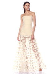 Woman wearing a strapless, light-colored evening gown with a floral skirt on a white background