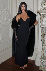 Woman in a black dress with a fur stole standing in an ornate room.