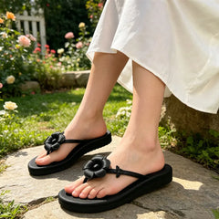 Feet wearing black satin flip flops with floral embellishments on stone steps.