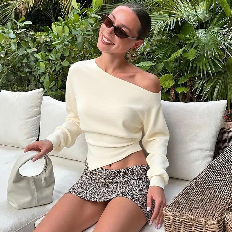 Woman in a white top and patterned shorts sitting on a couch with greenery in the background