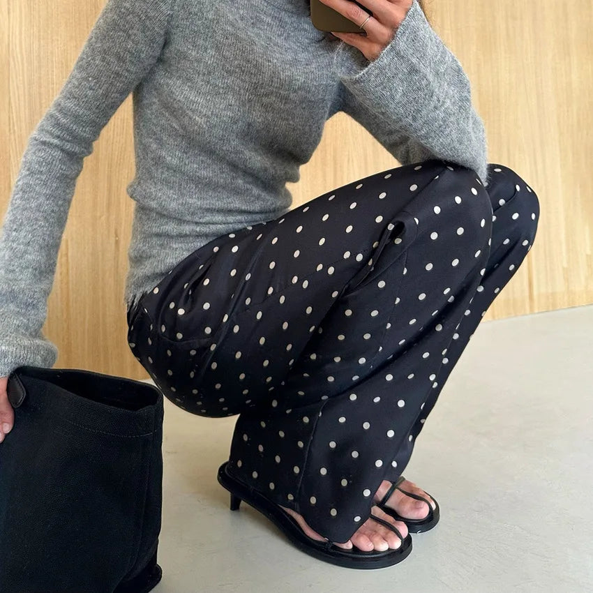 Person wearing black pants with white polka dots and a gray sweater, sitting on a light-colored surface.