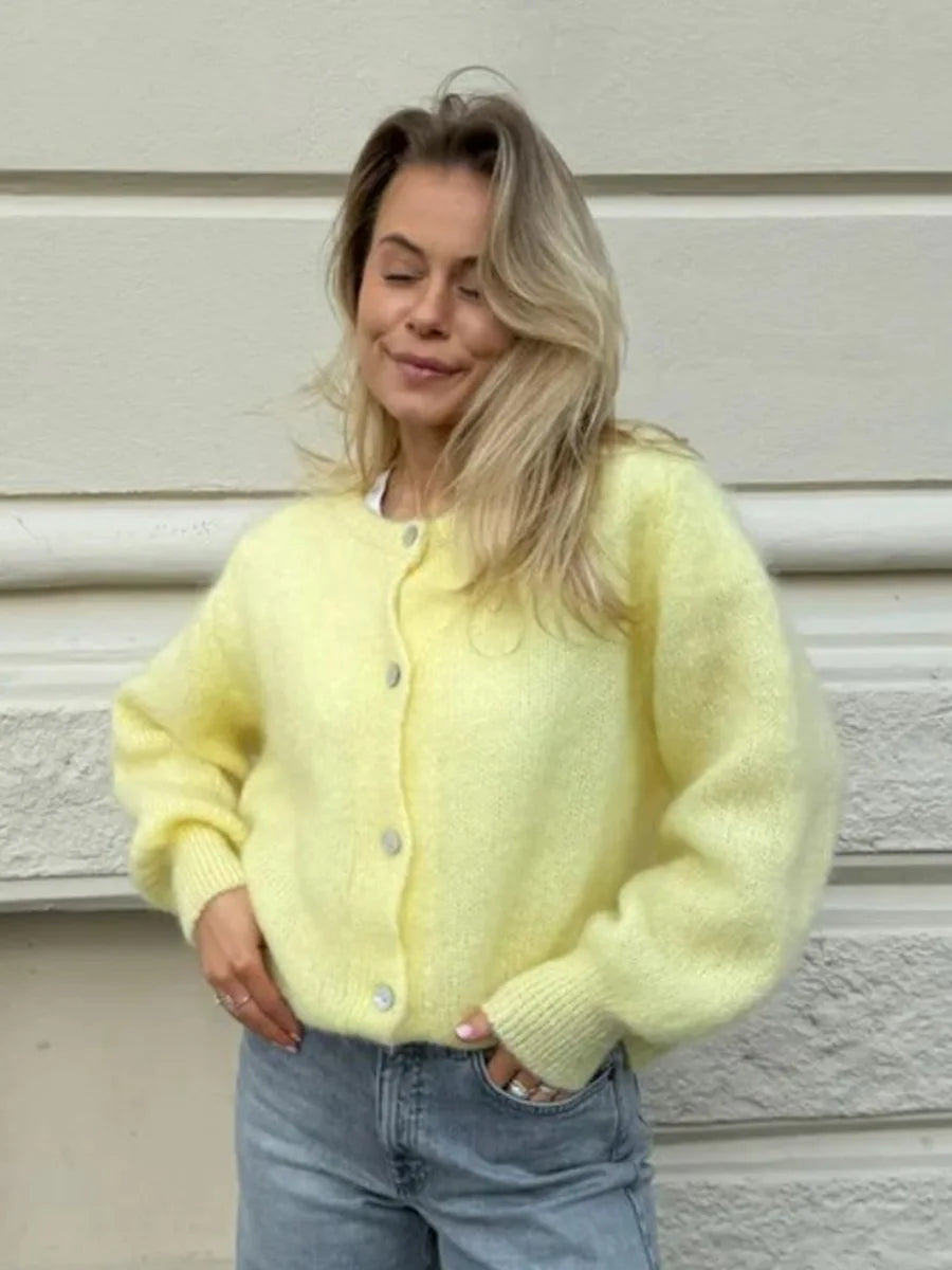 Woman wearing a light yellow cardigan and blue jeans against a neutral background