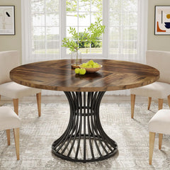 Round wooden dining table with black metal base in a bright room with chairs and decor.