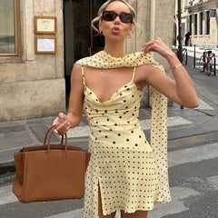Person posing in a polka dot cowl neck dress with a flowing scarf.