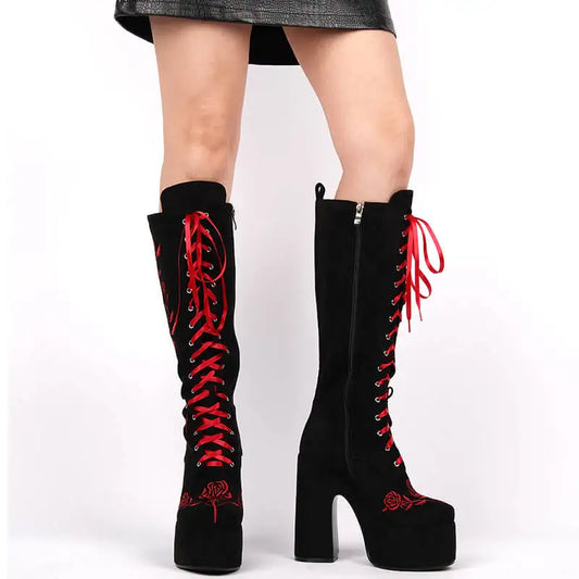Model wearing black knee-high platform boots with red floral embroidery and red lace-up detail