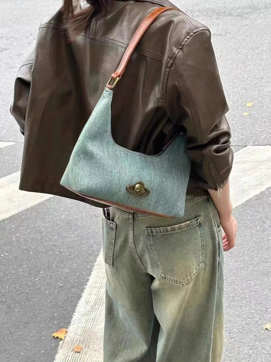 Person wearing a brown jacket and light blue denim bag on a street.