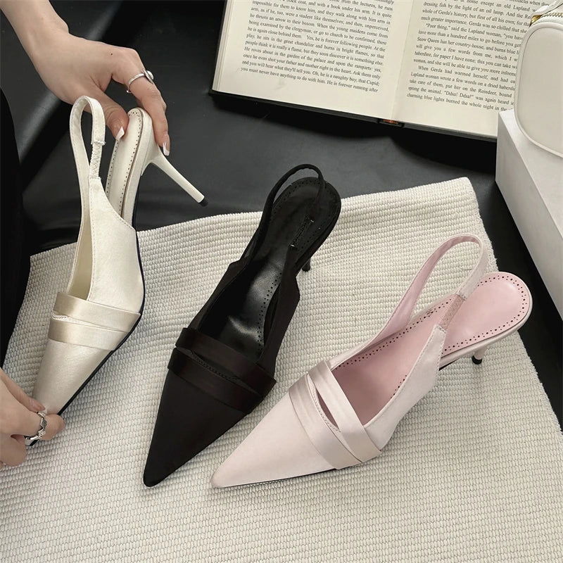 Three pairs of high-heeled shoes in white, black, and pink on a textured surface with a book in the background.