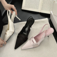 Three pairs of high-heeled shoes in white, black, and pink on a textured surface with a book in the background.