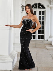 Woman in a black strapless dress with white embellishments standing in front of a white building.