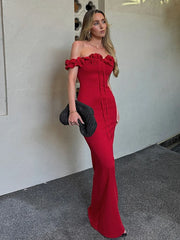 Woman in a red off-shoulder dress holding a black clutch against a neutral wall.