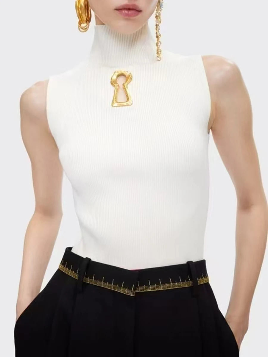 Person wearing a white sleeveless top with a gold brooch and black pants with gold trim on a light gray background