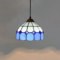 Golden Atelier pendant light featuring a handcrafted Tiffany glass shade with colorful stained glass panels, casting a warm glow. The light hangs from a chain on a ceiling in a living room setting. D