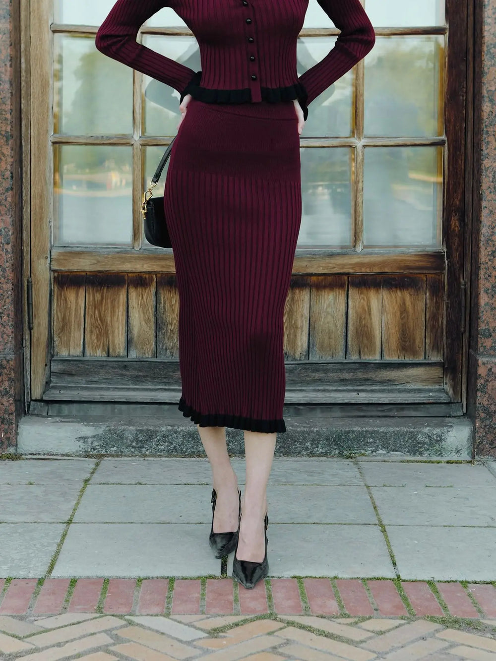 Person wearing a burgundy ribbed dress with black trim standing in front of a wooden door.