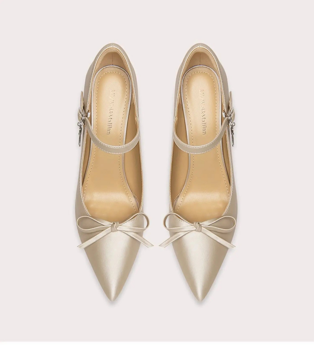 Pair of beige high-heeled shoes with bow details on a light gray background
