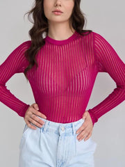 Woman wearing a pink ribbed long-sleeve top and light blue jeans against a plain background