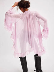 Person wearing a light pink ruffled blouse with long sleeves on a white background