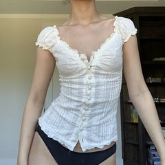 Person wearing a white lace top and black underwear in a room with a bookshelf.