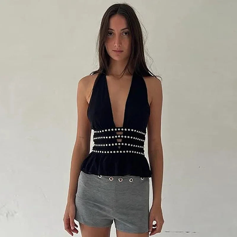 Woman wearing a black halter top with pearl details and gray shorts against a plain background