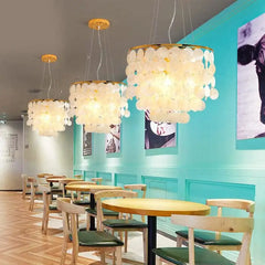 Modern restaurant interior with round tables, chairs, and decorative ceiling lights.
