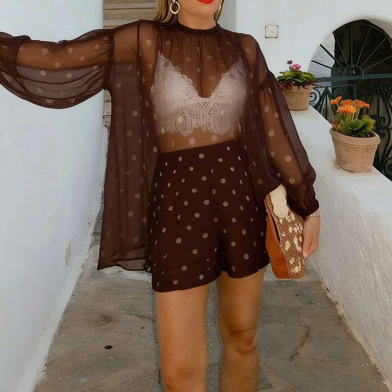 Woman wearing a brown polka dot outfit with sheer sleeves in an outdoor setting.