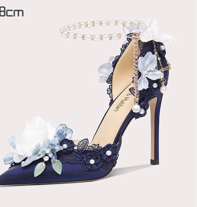 Navy blue high-heeled shoe with floral and pearl details on a white background