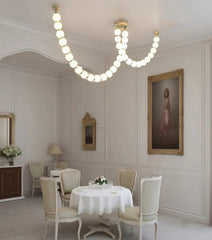 Sleek modern chandelier with LED lights, hanging above a dining room table. Golden Atelier 3