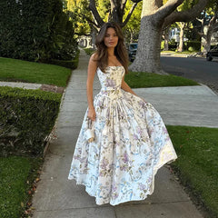 Woman in a floral dress walking on a sidewalk with trees and grass in the background