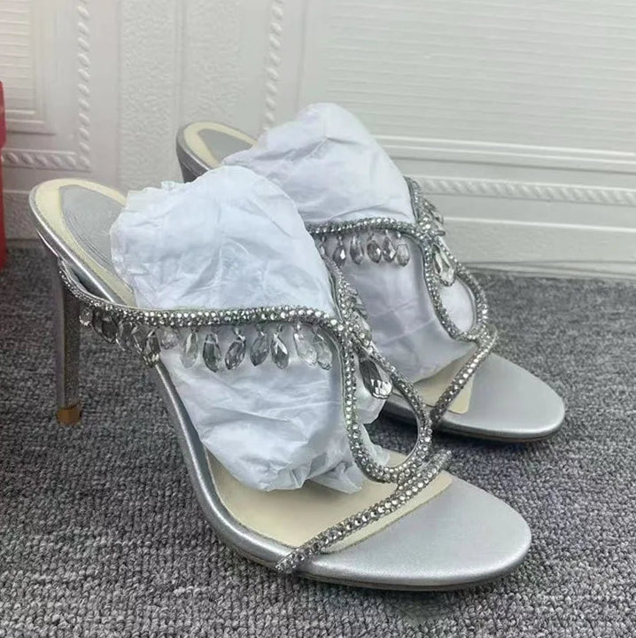 Silver high-heeled sandals with rhinestone embellishments on a carpeted floor.