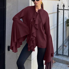 Woman wearing a burgundy ruffled blouse and black pants standing outside a building.