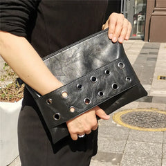 Person holding a black leather clutch with cut-out design on a city street.
