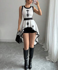 Woman wearing a white dress with black patterns and black knee-high boots in an indoor setting.
