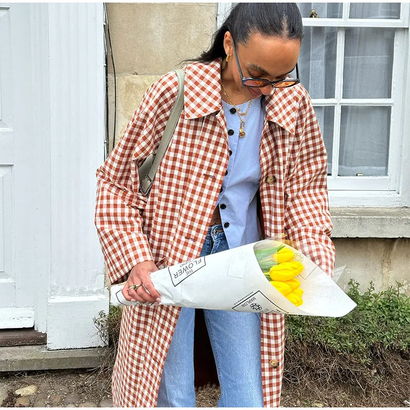 Person wearing a red and white checkered coat holding yellow flowers outdoors.